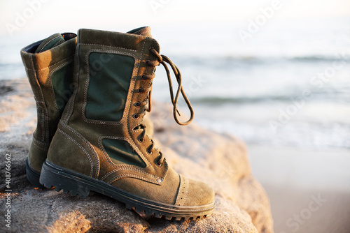 Men's army green boots with laces for outdoor activities stand on the background of the sea and stone