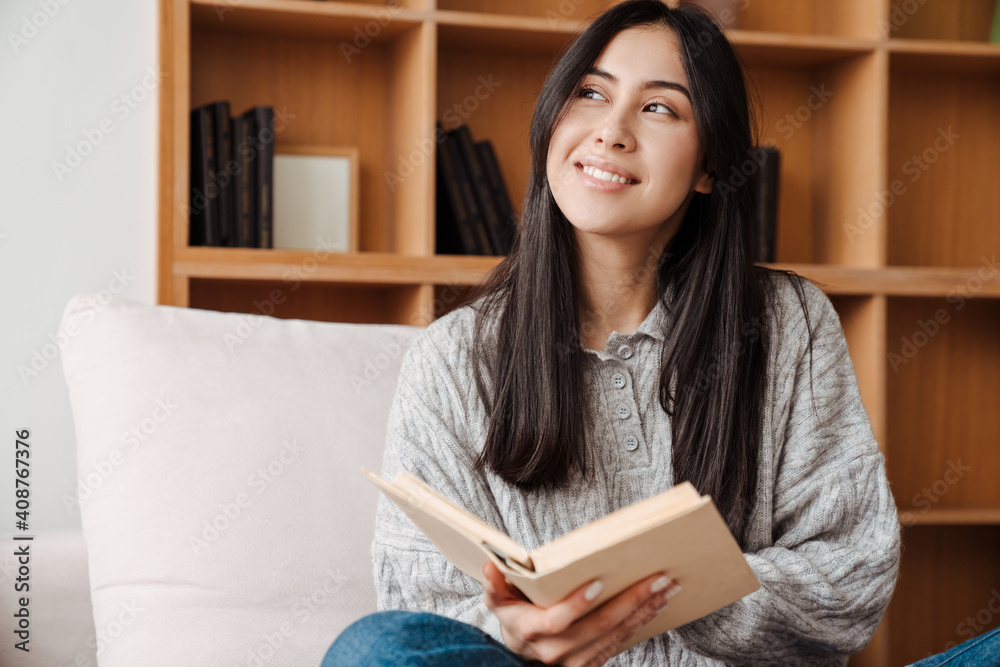 Young happy woman reading book while sitting on sofa Young happy woman reading book while sitting on sofa