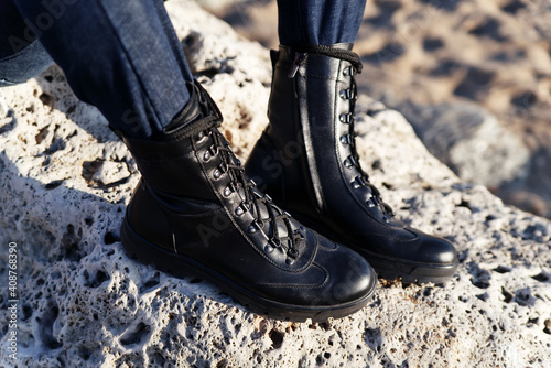 Black eco-leather military boots with laces for active tourism in the forest or mountains on a background of sand