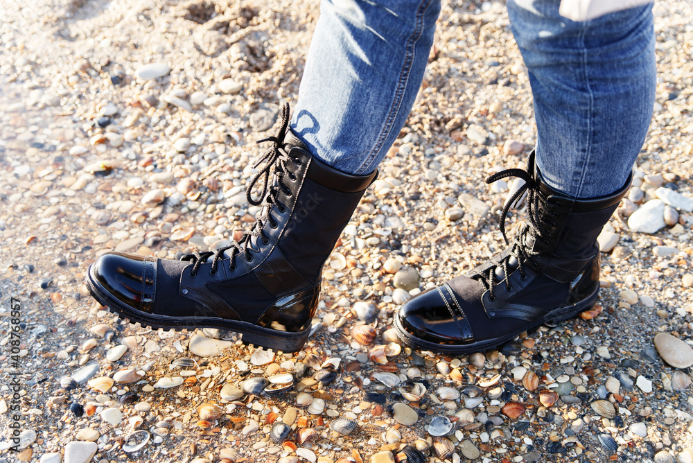 A man walks along the water and the shore in blue jeans and boots of black eco-leather with lace