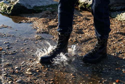 Man steps into the water with splashes in black unisex boots made of eco-leather on laces for climbing and fishing in the mountains