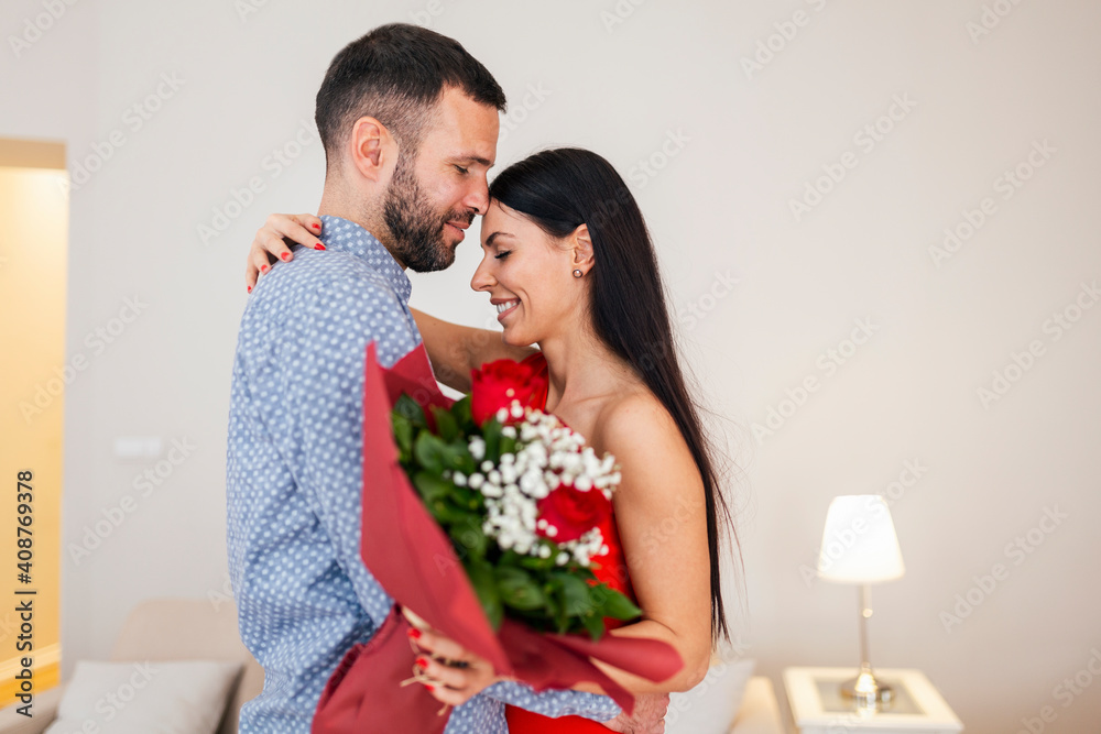 Valentine's Day concept. Happy couple in love with. A young loving couple celebrating Valentine's Day. Lovers hugging each other. Handsome man surprises his girlfriend with red roses at home