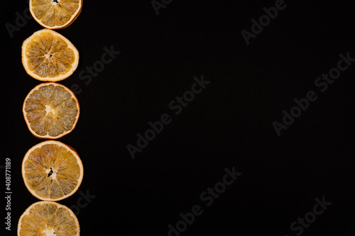 Sliced dried oranges in a raw on a left of black background, copy space, banner, free space for text, view from the top, no people.