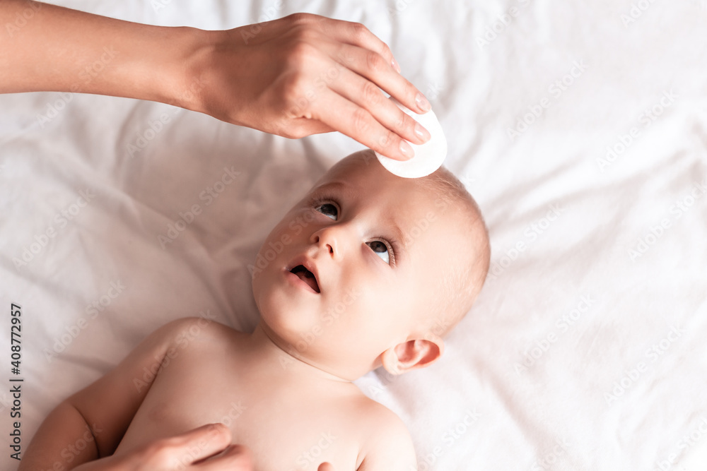 Concept Hygiene cleaning wipe, pure, clean. Mother's hand wiping newborn's face with white cotton pad. Wiping Baby's Face. Care about baby clean and soft body skin Concept Hygiene cleaning wipe, pure, clean. Mother's hand wiping newborn's face with white cotton pad. Wiping Baby's Face. Care about baby clean and soft body skin
