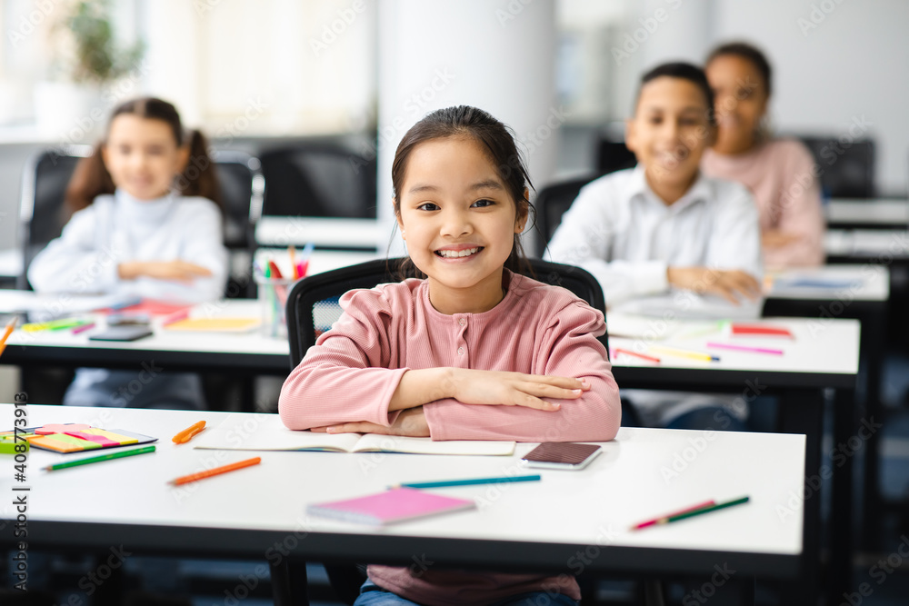 Portrait of small blackasian girl sitting at desk in classroom Portrait of small blackasian girl sitting at desk in classroom