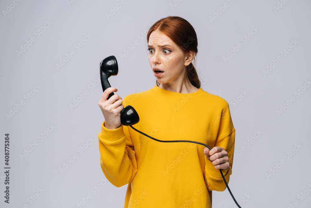 Scared shocked young woman wearing stylish yellow sweater talking on retro phone against isolated white background. Pretty redhead lady model emotionally showing facial expressions. Scared shocked young woman wearing stylish yellow sweater talking on retro phone against isolated white background. Pretty redhead lady model emotionally showing facial expressions.