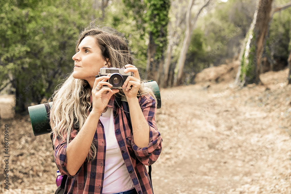 Pensive lady holding camera, looking around and standing on road. Female tourist exploring nature and taking photo of forest. Greenery on background. Tourism, adventure and summer vacation concept Pensive lady holding camera, looking around and standing on road. Female tourist exploring nature and taking photo of forest. Greenery on background. Tourism, adventure and summer vacation concept