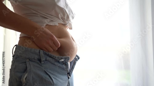 Close-up of a young woman touching her belly, trying to button up tight jeans. Overweight, diet and weight loss concept. Overweight woman