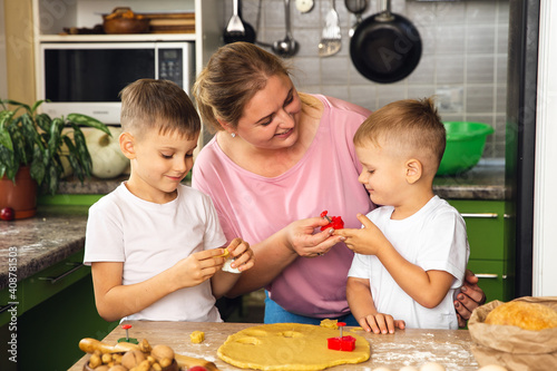 Caring mother help little preschooler sons prepare cookies, smiling loving mom learn cooking with small boys child, making lunch on weekend in kitchen together