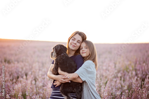 Two caucasian sisters hugging together in nature with a small black dog. Family and happines concept. Outdoors