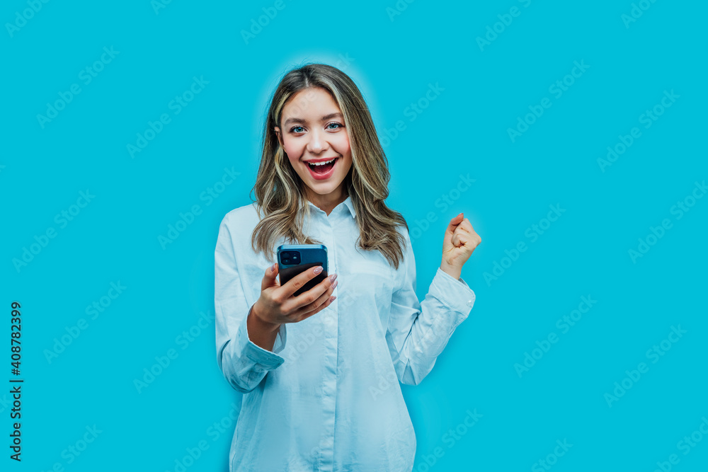 Attractive girl on a blue background with a phone in her hands, she is happy with the purchase she made online. Place for text, online shopping