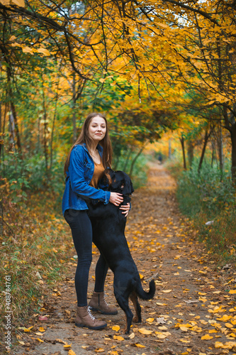 Beautiful caucasian woman with her big black dog are hugging on a checkered brown plaid in the autumn forest. Rottweiler with his owner is looking  into the camera. Pet loving and friendship concept. © Olga Pulchina