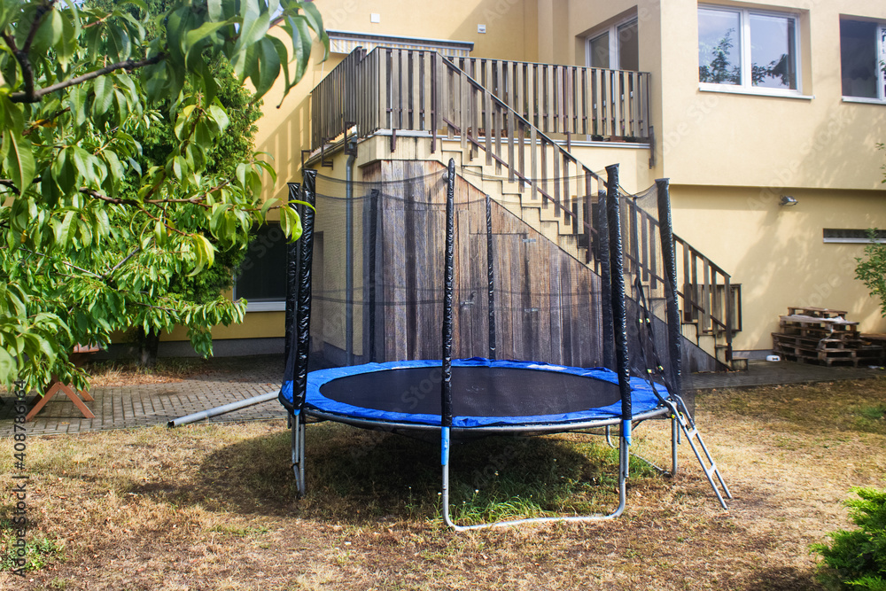 Trampoline with safety net on the lawn in a backyard. Front view of trampoline in a garden. Trampoline jumping.