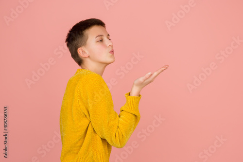 Sending kisses. Caucasian girl's portrait on coral pink studio background with copyspace for ad. Beautiful female model in sweater. Concept of human emotions, facial expression, sales, ad, fashion.