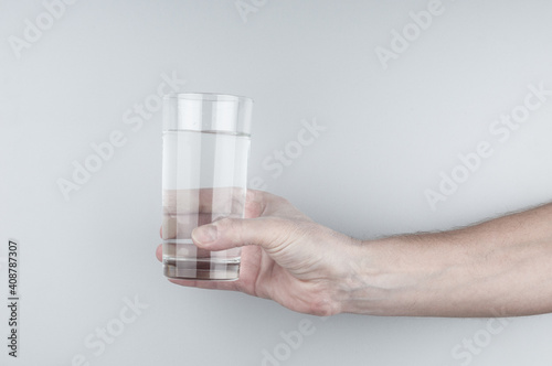 Hand holding glass of pure water on gray background