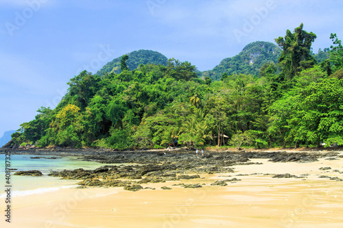 View over white sand and shallow water lagoon of tropical empty remote island beach with green hills jungle forest background - Koh Mook, Thailand