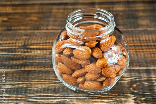 Almonds in a glass transparent jar. Nuts on an old shabby board. Jar on a brown wooden table close up. photo