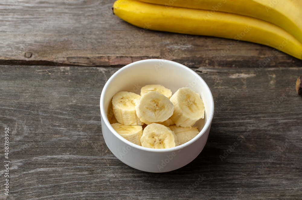 Slices of bananas in a white plate on a rustic wooden background preparing for cooking.