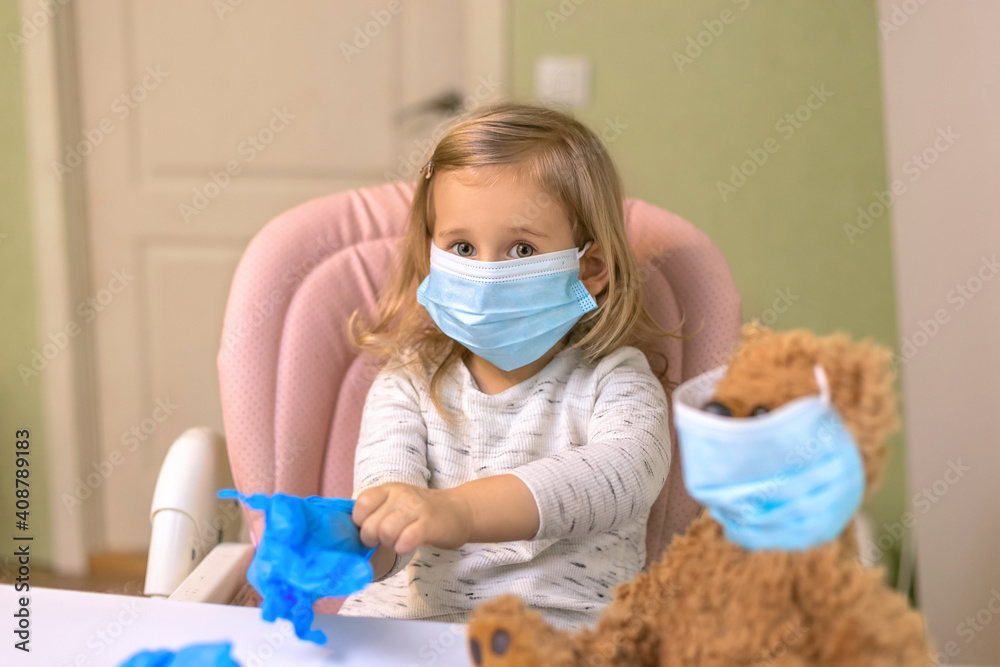 ittle girl playing doctor with her bear sitting near the table wearing a medical mask