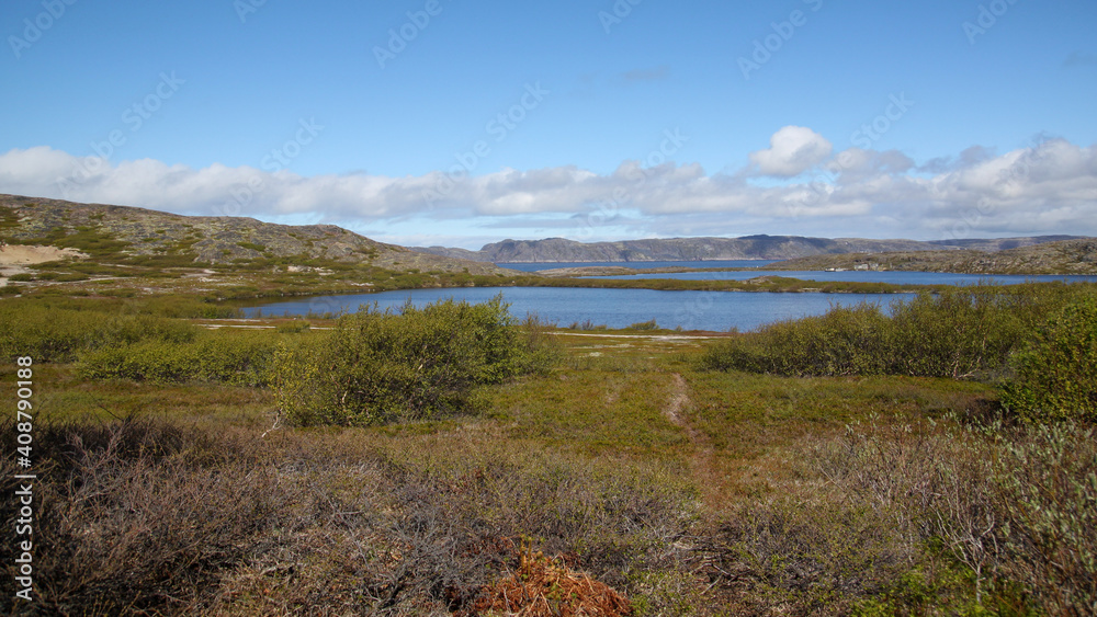 Blue lakes in the mountains. A path leading to the lakes. Green bushes and grass grow around the lakes. Stone hills are visible in the background. Beautiful white clouds float across the blue sky. Blue lakes in the mountains. A path leading to the lakes. Green bushes and grass grow around the lakes. Stone hills are visible in the background. Beautiful white clouds float across the blue sky.