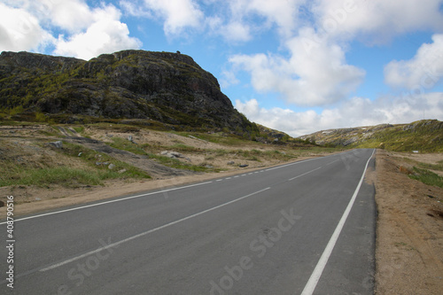 A asphalt road between the hills. The path that goes beyond the horizon. White clouds on a blue sky. Rural landscape.
