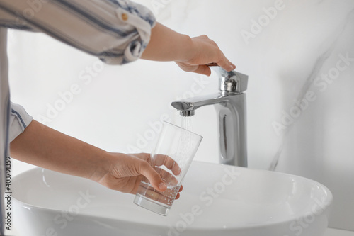 Woman filling glass with water from faucet over sink, closeup