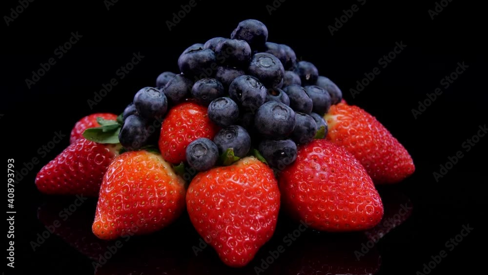 Strawberries and blueberries rotating on a black background. Fresh, organic vibrant red strawberry and blueberry in 4K. Raw vegan summer snack. Strawberries and blueberries rotating on a black background. Fresh, organic vibrant red strawberry and blueberry in 4K. Raw vegan summer snack.