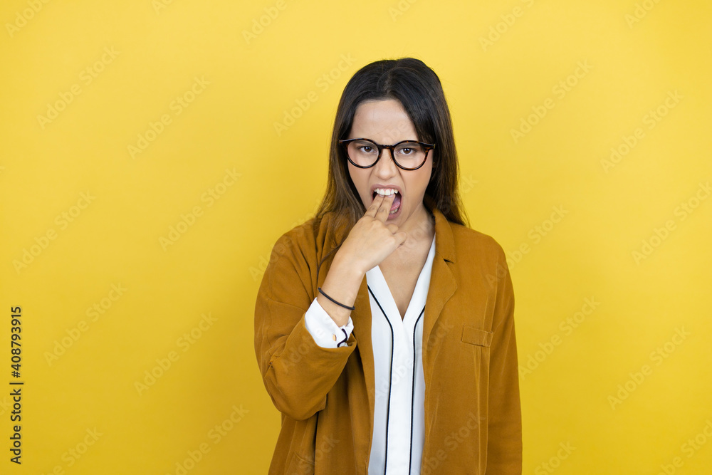 Young beautiful woman wearing a blazer over isolated yellow background disgusted with her hand inside her mouth