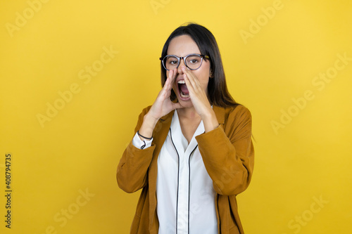 Young beautiful woman wearing a blazer over isolated yellow background shouting and screaming loud to side with hands on mouth