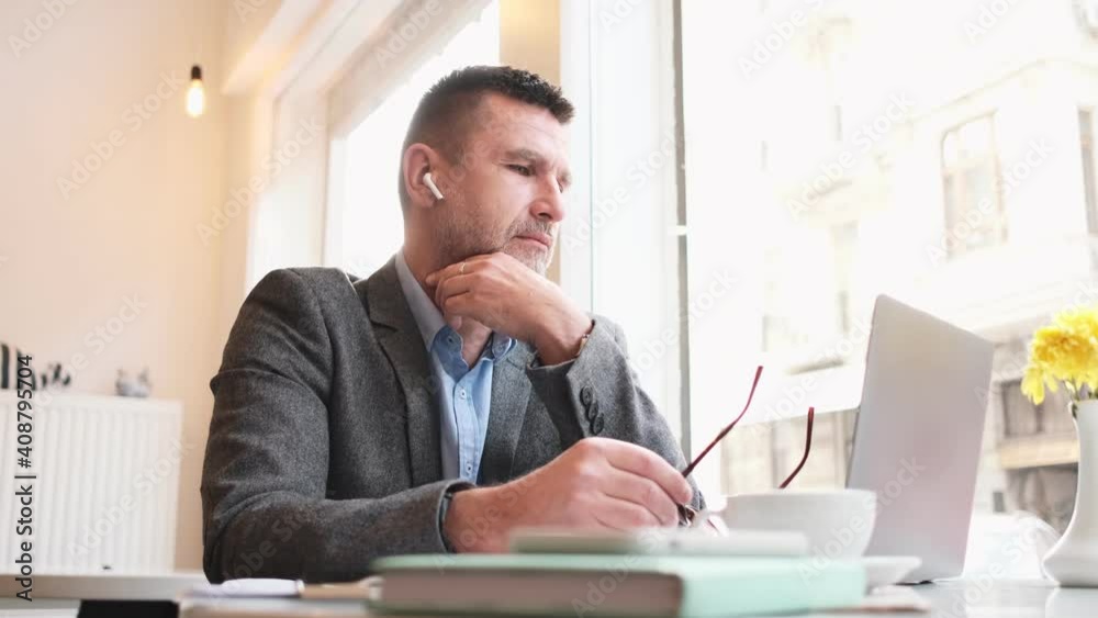 A thinking adult man is working with his laptop computer sitting at the table in a cafe A thinking adult man is working with his laptop computer sitting at the table in a cafe