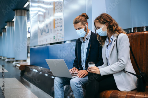 young couple in protective masks using a laptop on the subway platform .