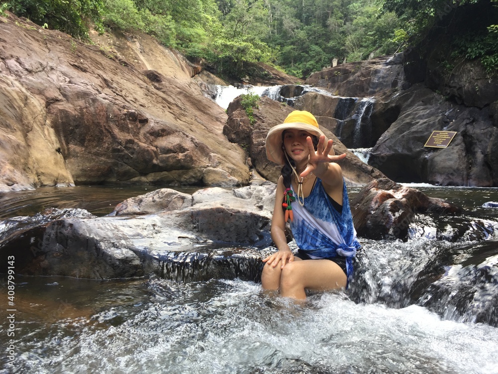 Fototapeta premium A woman in a yellow hat is climbing a rock in the middle of the river.