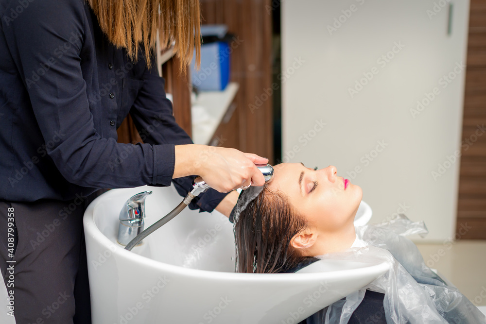 Naklejka premium A female hairdresser is rinsing the hair of a young woman in a sink after shampooing in a hair salon