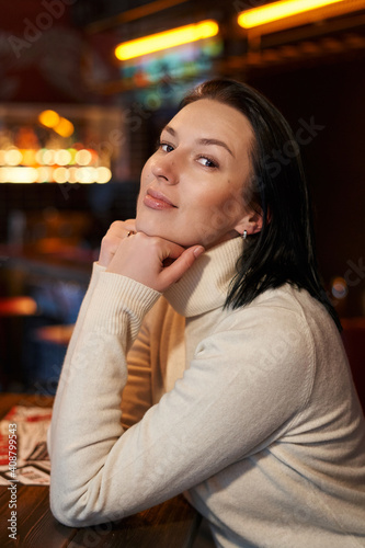 beautiful smiling girl with shoulder-length dark hair sits in a cafe  propping her head with both hands