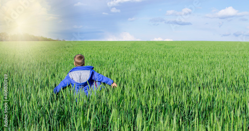 Happy boy walks across a green field with his arms spread.