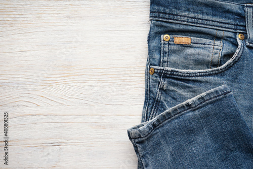 Folded denim pants on a wooden background, space for text. Top view.