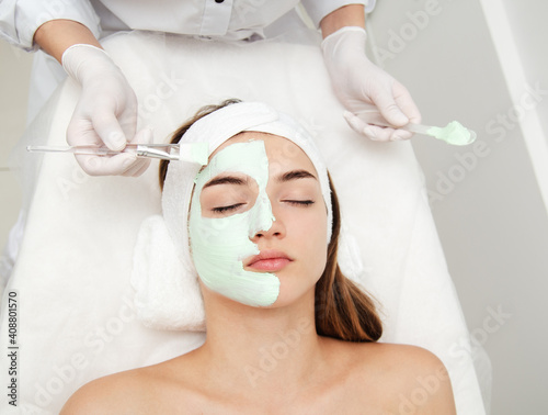 Beautiful young woman with facial mask in beauty salon. Girl getting beauty treatment facial care