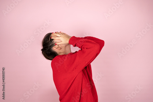 Woman in red sweater covering her face with hands. Concept of fear, shame, domestic violence.