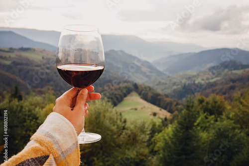 Woman's hand holding a glass of red wine with a mountain view. photo