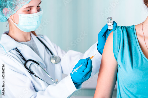 Doctor or nurse in uniform and gloves wearing face mask protective in lab making an injecion holding vaccine bottle with COVID-19 Coronovirus vaccine label