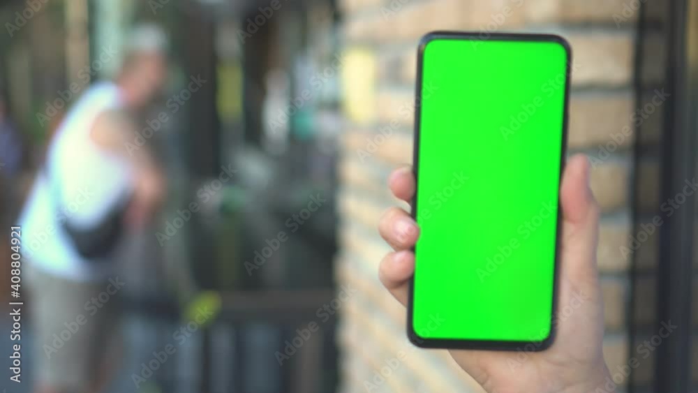 Close up hands woman holding phone with vertical green screen on busy street background pavement scrolling pages swiping surfing internet technology chroma key message Close up hands woman holding phone with vertical green screen on busy street background pavement scrolling pages swiping surfing internet technology chroma key message