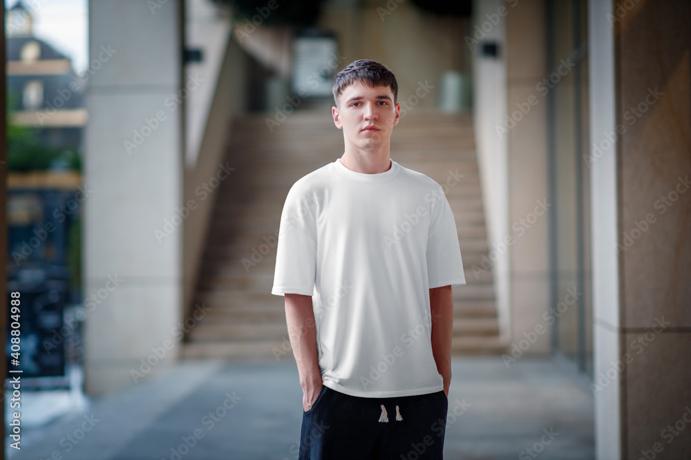 White T-shirt template on a guy, against the background of a blurred building, urban clothing style, for advertising in an online store. White T-shirt template on a guy, against the background of a blurred building, urban clothing style, for advertising in an online store.