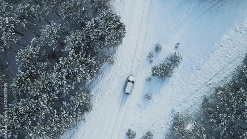 Aerial top view from drone of suv vehicle driving on snowy ice road exploring local landscapes in winter