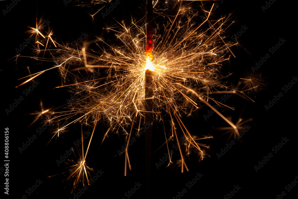 Horizontal conceptual close-up photo of an isolated 
sparkler in the process emitting a lot of bright sparks in the dark
