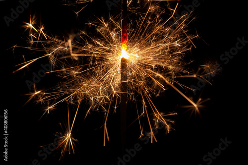 Horizontal conceptual close-up photo of an isolated  sparkler in the process emitting a lot of bright sparks in the dark