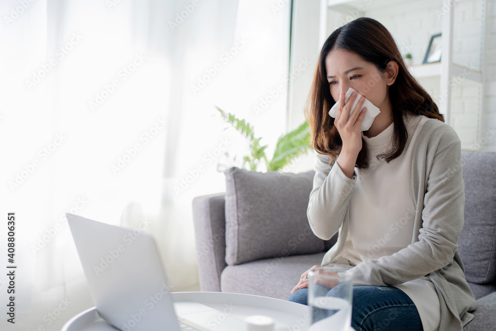 Young Asian women cough and sneeze while working at home. She feels sick. Young Asian women cough and sneeze while working at home. She feels sick.