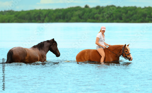 Caucasian woman is bathing two horses in water in outdoors.