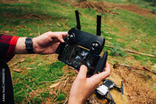 Hands of a young man on a remote control to control a drone on a background of moss in the woods. Using a drone on a hike.