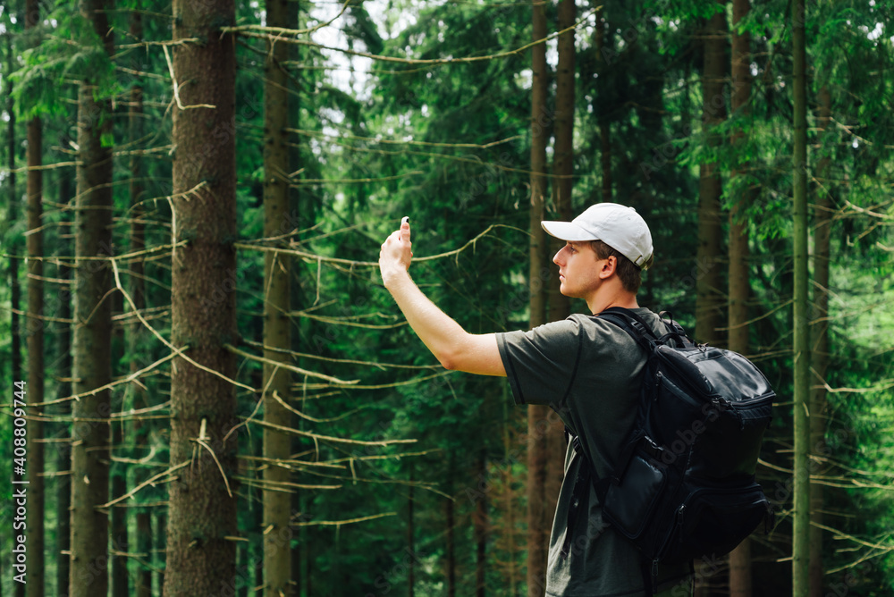 A young man catches a cellular network on a smartphone while walking in the mountains, stands in a beautiful coniferous forest and uses a smartphone. A young man catches a cellular network on a smartphone while walking in the mountains, stands in a beautiful coniferous forest and uses a smartphone.