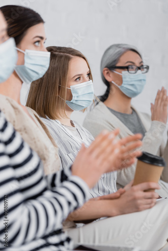 multiethnic businesswomen in medical masks applauding and looking away during seminar